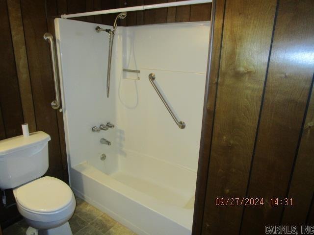 bathroom with wooden walls, toilet, and shower / bathtub combination