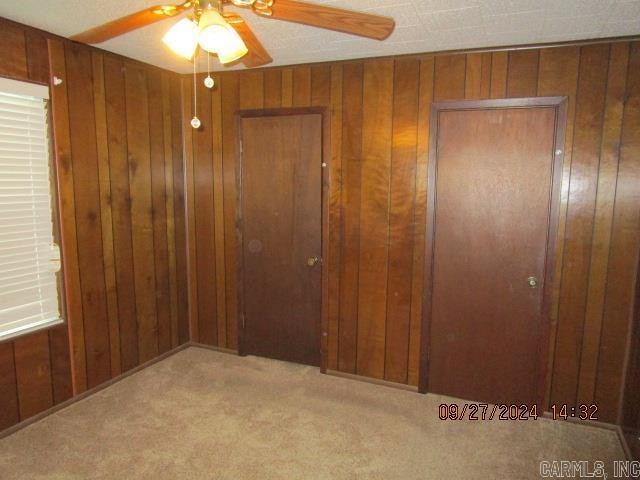 spare room with ceiling fan, light colored carpet, a textured ceiling, and wood walls