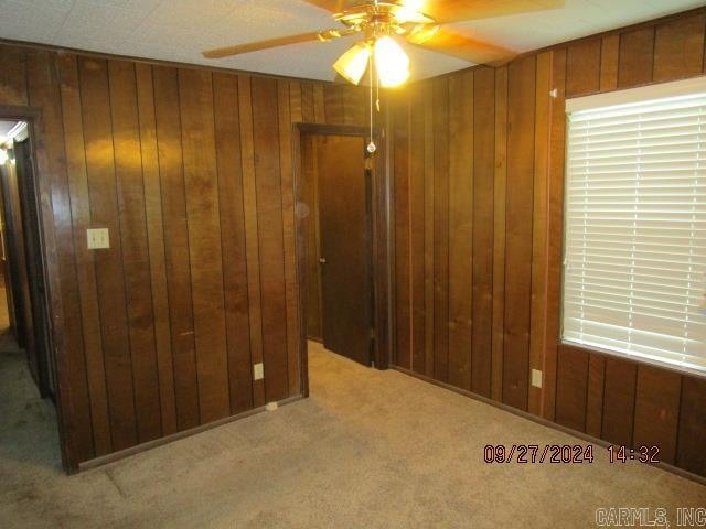 carpeted empty room featuring ceiling fan and wooden walls