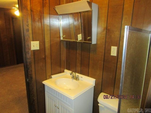 bathroom featuring wooden walls, toilet, and vanity