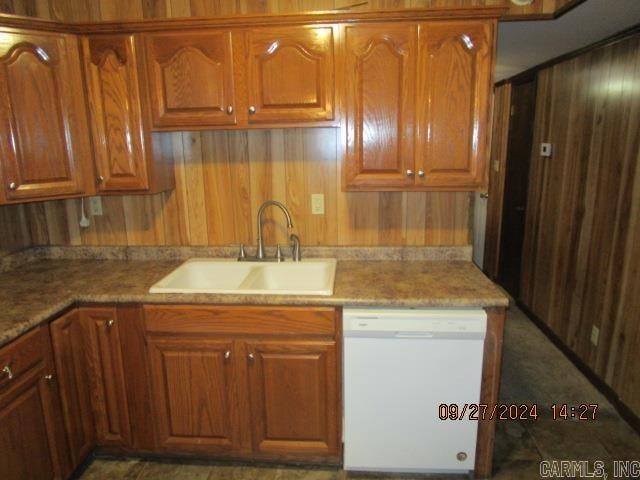 kitchen with wood walls, sink, white dishwasher, and light stone counters