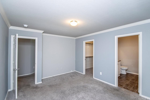 unfurnished bedroom with a textured ceiling, crown molding, ensuite bathroom, a walk in closet, and light colored carpet