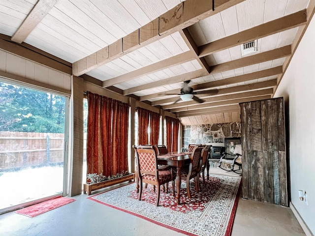 dining room with vaulted ceiling with beams, concrete flooring, ceiling fan, and a stone fireplace