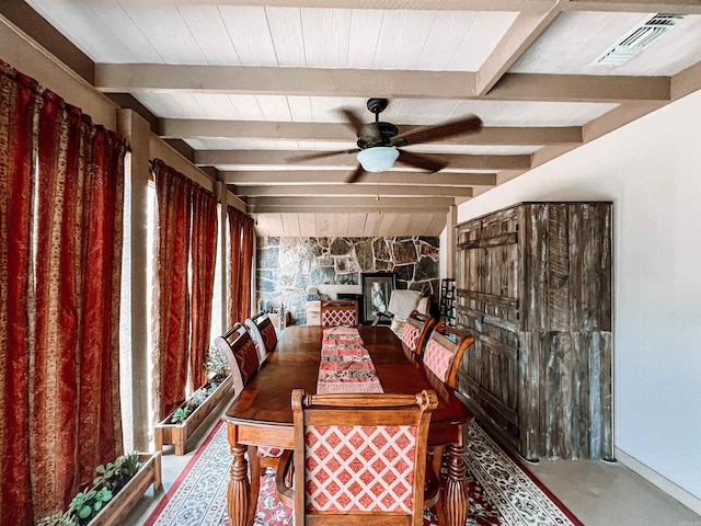 unfurnished dining area with ceiling fan, beamed ceiling, a fireplace, and concrete flooring