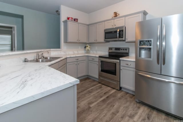 kitchen with kitchen peninsula, dark hardwood / wood-style flooring, gray cabinets, stainless steel appliances, and sink