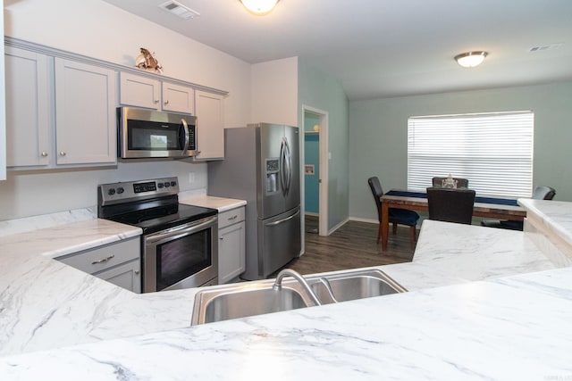 kitchen with gray cabinetry, light stone counters, appliances with stainless steel finishes, and dark wood-type flooring