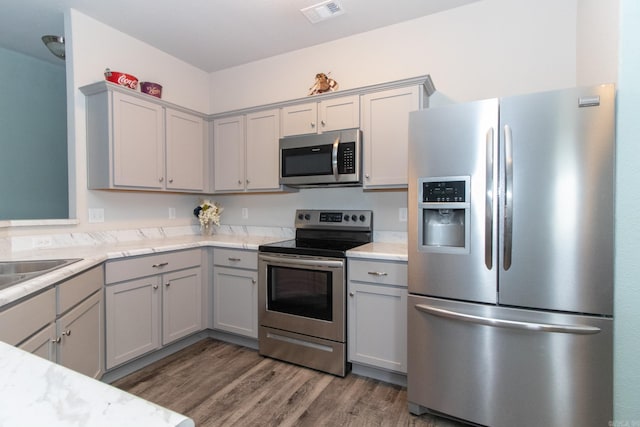 kitchen featuring gray cabinetry, dark hardwood / wood-style floors, stainless steel appliances, and light stone countertops