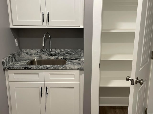 interior space featuring dark stone counters, white cabinetry, sink, and wood-type flooring