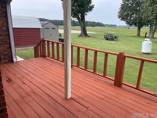 wooden terrace featuring a storage unit, a rural view, and a lawn