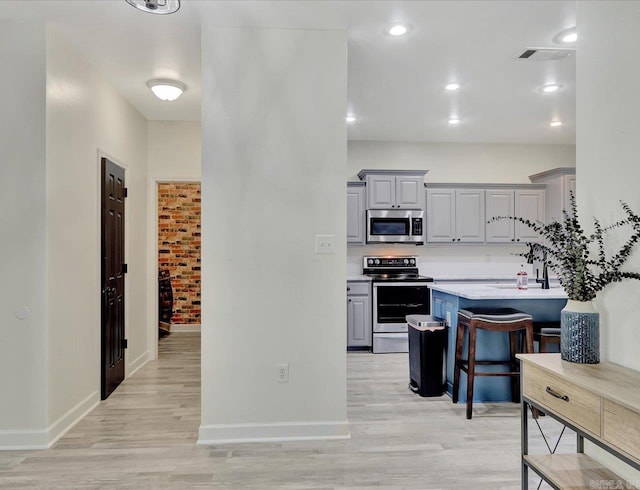 kitchen with gray cabinets, appliances with stainless steel finishes, light wood-type flooring, and a kitchen bar