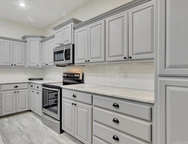 kitchen featuring appliances with stainless steel finishes, light hardwood / wood-style floors, backsplash, light stone countertops, and gray cabinets