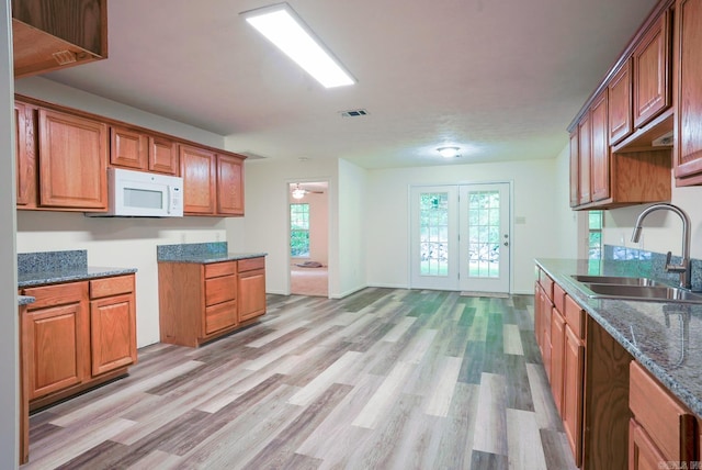 kitchen with light hardwood / wood-style flooring, dark stone countertops, sink, and ceiling fan