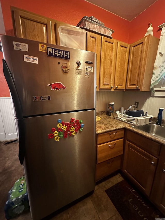 kitchen with dark tile patterned flooring, brown cabinets, a sink, and freestanding refrigerator