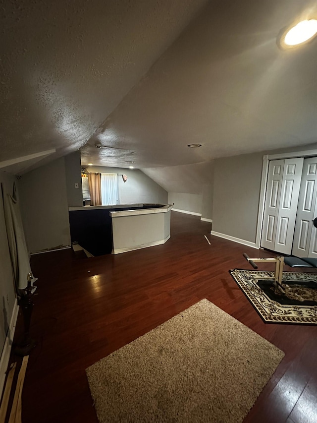 bonus room with dark wood-style flooring, vaulted ceiling, a textured ceiling, and baseboards