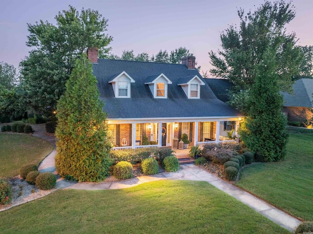 cape cod house featuring a lawn and covered porch