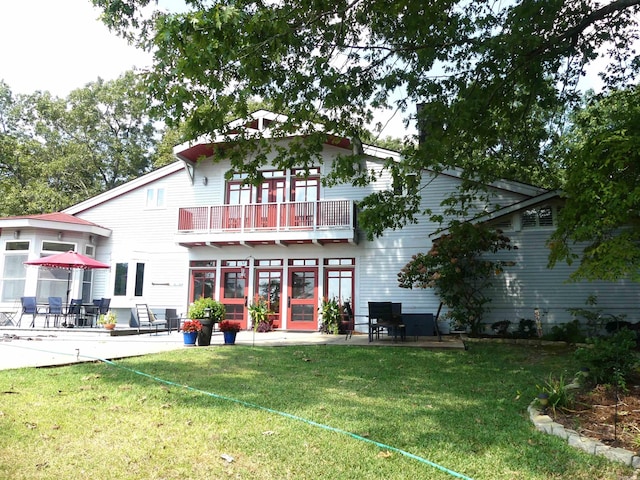 rear view of house featuring a patio area, a balcony, and a lawn