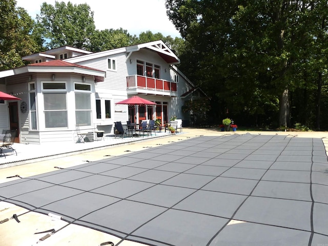 back of property featuring a balcony, a covered pool, and a patio area