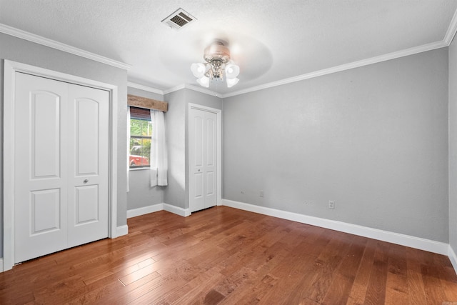 unfurnished bedroom featuring a closet, a textured ceiling, hardwood / wood-style floors, ornamental molding, and ceiling fan