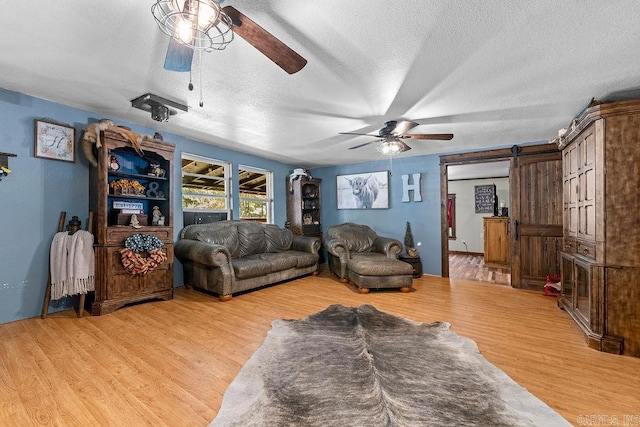 living room featuring ceiling fan, a barn door, light hardwood / wood-style floors, and a textured ceiling