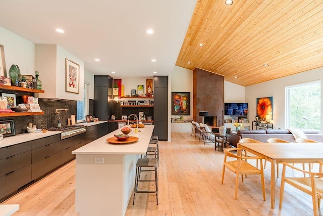 kitchen with wood ceiling, a kitchen island with sink, a breakfast bar, light wood-type flooring, and vaulted ceiling