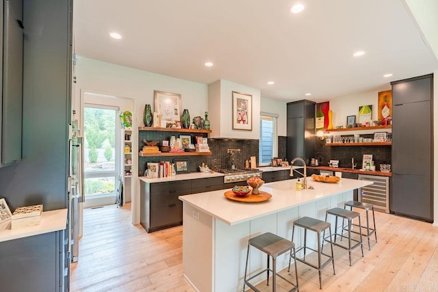 kitchen featuring sink, beverage cooler, a kitchen bar, backsplash, and a center island with sink