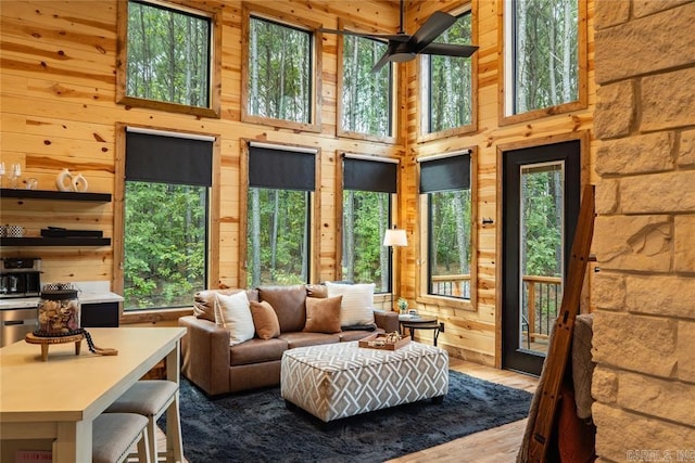 living room featuring ceiling fan, wooden walls, hardwood / wood-style floors, and a high ceiling