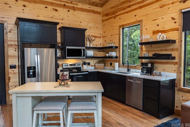 kitchen featuring appliances with stainless steel finishes, light wood-type flooring, a kitchen bar, wooden walls, and sink