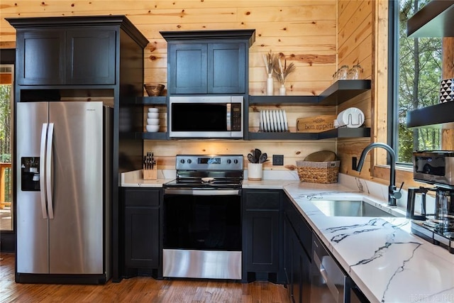 kitchen with hardwood / wood-style flooring, appliances with stainless steel finishes, wood walls, and sink