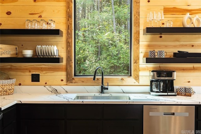 kitchen with light stone countertops, dishwasher, wood walls, and sink