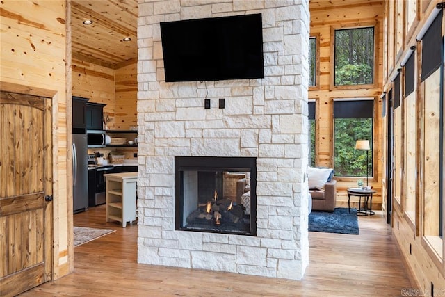 living room featuring wood-type flooring, a stone fireplace, wood walls, and high vaulted ceiling