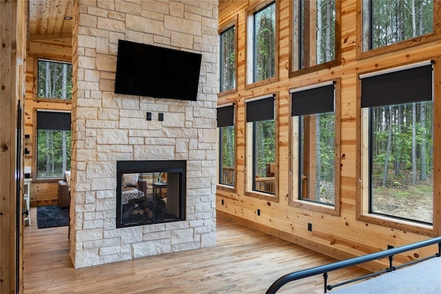 unfurnished living room with a high ceiling, a stone fireplace, wooden walls, and light hardwood / wood-style flooring