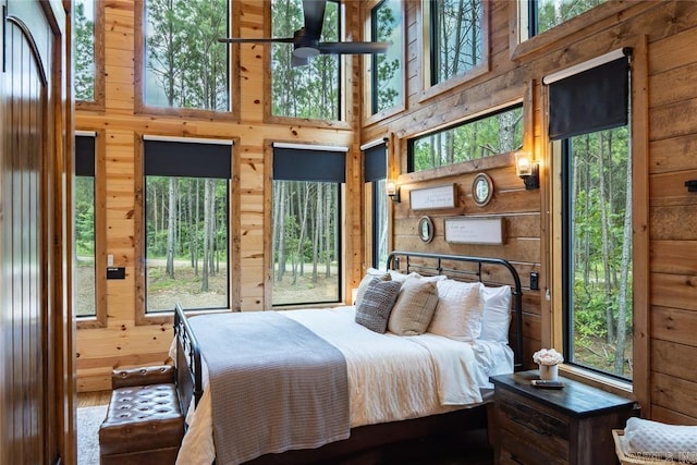 bedroom with multiple windows, a high ceiling, and wood walls