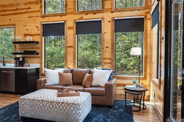 living room with light hardwood / wood-style flooring, wooden walls, a towering ceiling, and a healthy amount of sunlight