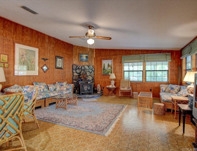 living room featuring a wood stove, ceiling fan, a healthy amount of sunlight, and a textured ceiling