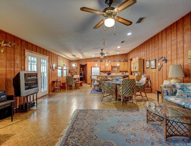 living room with ceiling fan, a textured ceiling, lofted ceiling, and wood walls