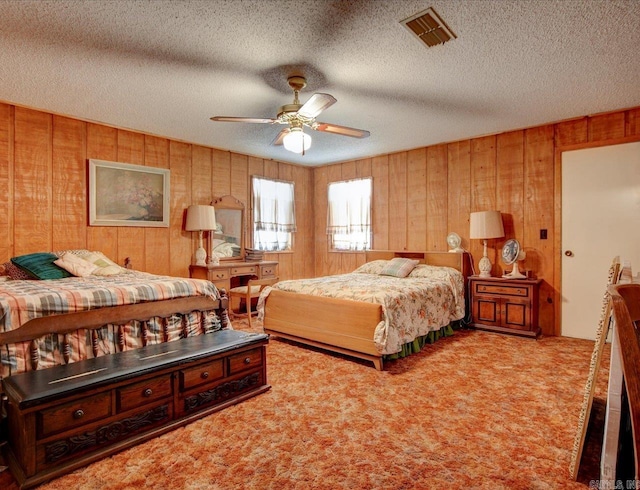 bedroom with ceiling fan, a textured ceiling, wooden walls, and carpet