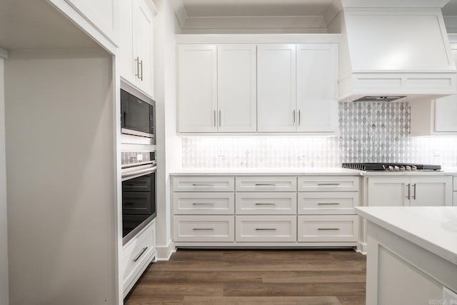 kitchen with dark hardwood / wood-style floors, backsplash, appliances with stainless steel finishes, white cabinetry, and premium range hood