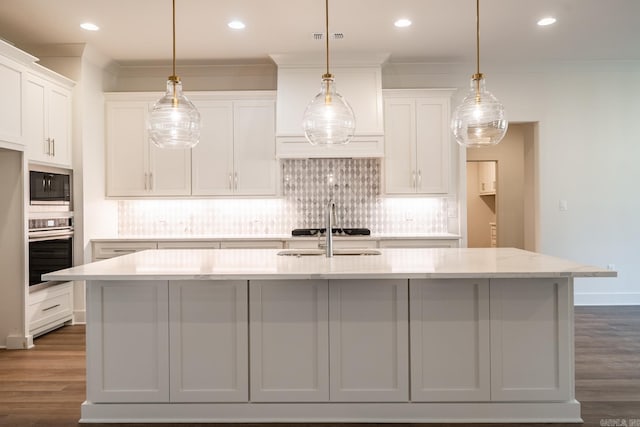 kitchen featuring dark wood-type flooring, a center island with sink, decorative light fixtures, white cabinetry, and appliances with stainless steel finishes