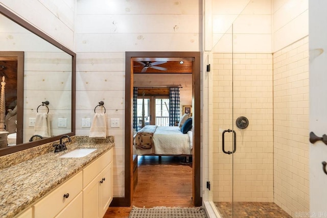 bathroom featuring wood walls, vanity, ceiling fan, a shower with door, and hardwood / wood-style floors