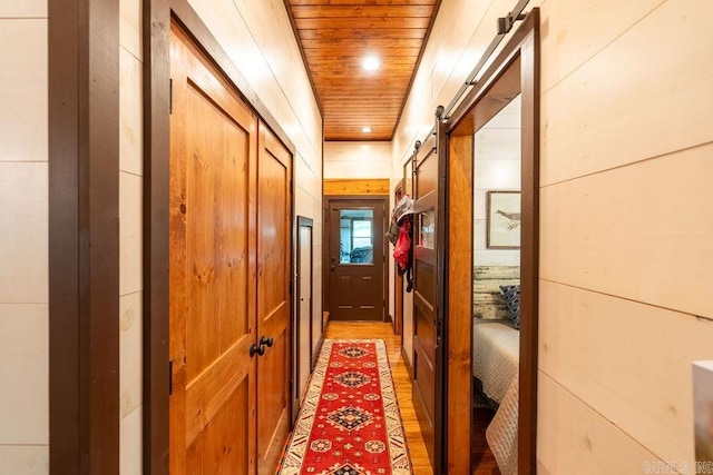 hallway with light hardwood / wood-style floors, wood walls, a barn door, and wood ceiling