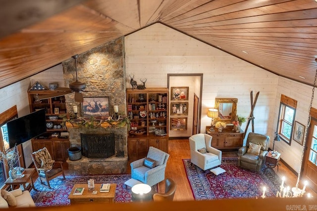 living room with lofted ceiling, wood walls, hardwood / wood-style flooring, and a stone fireplace