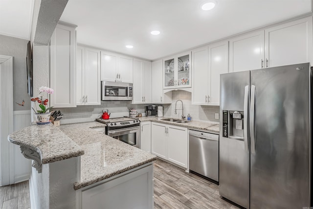 kitchen featuring sink, kitchen peninsula, white cabinetry, appliances with stainless steel finishes, and light stone countertops