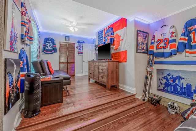 living room with a textured ceiling, wood-type flooring, ornamental molding, and ceiling fan