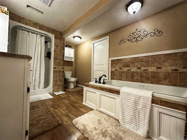 bathroom featuring wood-type flooring, tile walls, a textured ceiling, a tub to relax in, and toilet