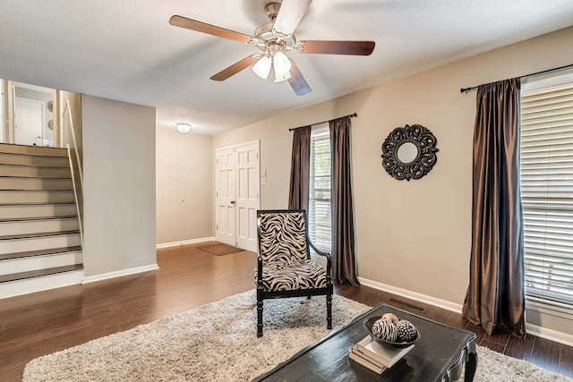 living area with ceiling fan, dark wood-type flooring, and a textured ceiling