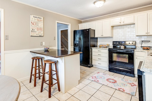 kitchen featuring black appliances, a kitchen bar, decorative backsplash, and white cabinets