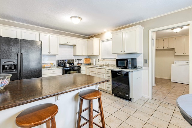 kitchen featuring light tile patterned flooring, white cabinets, black appliances, washer / dryer, and sink