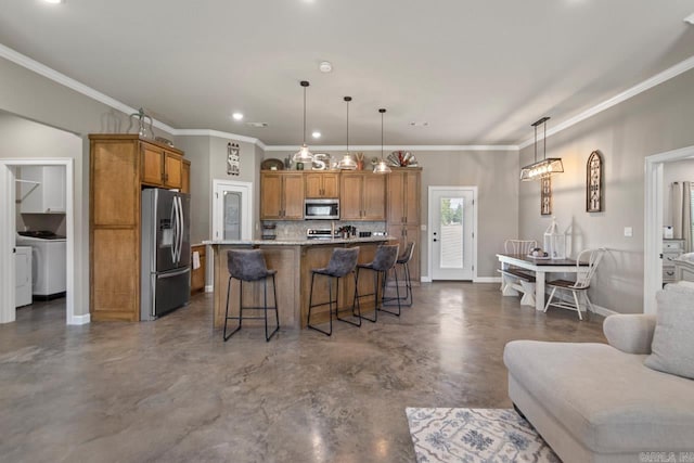 kitchen featuring washer / clothes dryer, an island with sink, pendant lighting, a kitchen bar, and appliances with stainless steel finishes