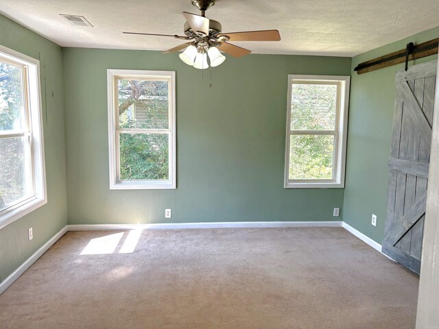 empty room featuring light carpet, a wealth of natural light, ceiling fan, and a barn door