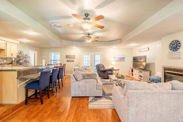 living room with a tray ceiling, a textured ceiling, light hardwood / wood-style flooring, ceiling fan, and french doors